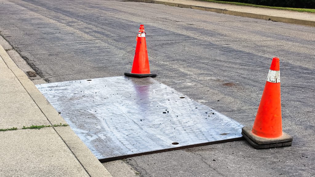 A,Steel,Plate,On,The,Road,With,Construction,Pylons.